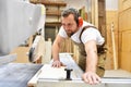 friendly carpenter with ear protectors and working clothes working on a saw in the workshop