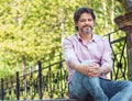 Friendly casual adult man sitting in the nature. Good looking businessman in park