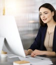 Friendly casual dressed business woman is working on her computer, while sitting at the desk in sunny office. Concept of