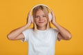 Friendly caucasian adolescent girl in white t-shirt in wireless headphones listening music, have fun alone