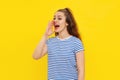 Friendly cheerful brunette girl shouting and screaming loud to side with hand on mouth, standing in white-blue striped t shirt Royalty Free Stock Photo