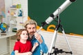 Friendly child in classroom near blackboard desk. Pupil watching stars with a teacher. Astronomy telescope.