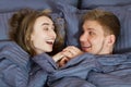 Friendly couple laughing out loud under the blanket lying on the bed - couple in bed