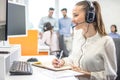 Friendly customer support operator woman in headset listening to a client and writing notes to notebook in call center. Royalty Free Stock Photo