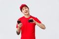 Friendly delivery guy in red uniform t-shirt and cap, showing smartphone screen and credit card, recommend application