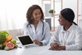 Friendly dietologist showing black lady patient empty digital tablet screen