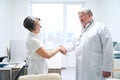 Friendly doctor greets with handshake elderly woman in medical office