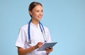 Friendly doctor nurse with tablet wireless computer smiles in isolated against blue background