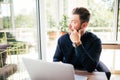 Friendly executive sitting in front of laptop in his office. Big window at the background. Looking away, daydreaming Royalty Free Stock Photo