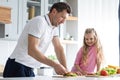 A friendly family from father with daughter stand and manage in the kitchen. A young serious man dad gives his child