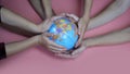 A friendly family hold the earth globe in their hands on a pink background. The concept of saving the world. Royalty Free Stock Photo