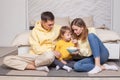 Friendly family, lovely parents in yellow clothes with child son sitting by the bed and holding bowl with popcorn Royalty Free Stock Photo