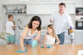 Friendly family tidy up room together. Mom and daughter are dusting the table. Father and son vacuuming room