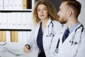 Friendly female doctor sitting in clinic with her male colleague at the background. Perfect medical service and medicine Royalty Free Stock Photo