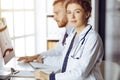 Friendly female doctor sitting in clinic with her male colleague at the background. Perfect medical service and medicine Royalty Free Stock Photo