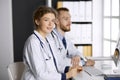 Friendly female doctor sitting in clinic with her male colleague at the background. Perfect medical service and medicine Royalty Free Stock Photo