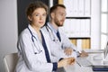 Friendly female doctor sitting in clinic with her male colleague at the background. Perfect medical service and medicine Royalty Free Stock Photo