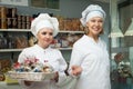 Friendly female staff in white robes offering sweets in confectionery Royalty Free Stock Photo