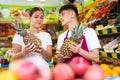 Friendly guy seller helps a girl buyer choose a pineapple