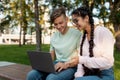 Friendly international college classmates preparing for lectures outdoors, sitting in park or college campus with laptop