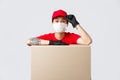 Friendly-looking asian delivery guy in red cap and t-shirt, courier service lean on cardboard box or client package