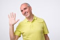 Friendly-looking attractive european man waiving hand in hello gesture while smiling cheerfully.