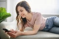 friendly looking long-haired girl using cellphone sitting at home on couch