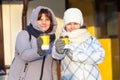 Friendly looking women holds disposable cups of coffee, suggests to drink together, focus is on paper cups