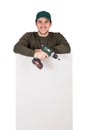 Friendly maintenance worker with a screwdriver or electric drill in his hand, stands behind a white panel. Man installing interior