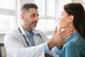 Friendly middle aged male doctor checking sore throat or thyroid glands, touching neck of young female patient Royalty Free Stock Photo