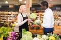 Friendly middle aged saleswoman helping African man to choose fresh cabbage in organic food store