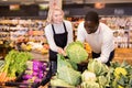 Friendly middle aged saleswoman helping African man to choose fresh cabbage in organic food store