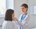 Middle-aged woman doctor wearing gloves checking patients sore throat or thyroid glands