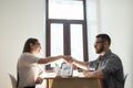 Friendly millennial coworkers handshaking over office desk. Busi