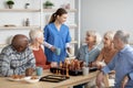 Friendly nurse holding mugs, talking to elderly people, serving tea Royalty Free Stock Photo
