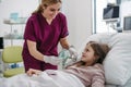 Friendly nurse putting oxygen mask on little patient face. Cute girl lying in hospital bed, smiling at doctor, trusting Royalty Free Stock Photo