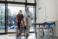 Friendly pediatrician nurse talking, pushing little patient in wheelchair. Cute preschool girl trusting her doctor and Royalty Free Stock Photo