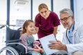 Friendly pediatrician showing someting on tablet to little patient in wheelchair. Cute preschool girl trusting her Royalty Free Stock Photo