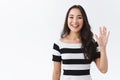 Friendly, pleasant and cheerful east-asian woman in striped t-shirt raising palm, wave hand greeting, saying hi or hello