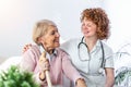 Friendly relationship between smiling caregiver in uniform and happy elderly woman. Supportive young nurse looking at senior woman Royalty Free Stock Photo