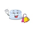 A friendly rich blueberry macaron waving and holding Shopping bag
