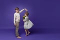 Friendly romantic dance of cute couple boy and girl small smiling children on purple background. Kids wearing casual beige clothes Royalty Free Stock Photo