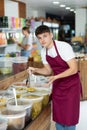 Friendly salesman in an apron offers to buy pickled green olives in grocery supermarket