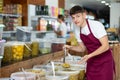 Friendly salesman in an apron offers to buy pickled green olives in grocery supermarket