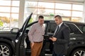 friendly salesman with male client talking and explaining new car before sale or rent in dealership