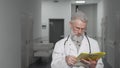 Friendly senior doctor smiling to the camera standing at hospital hallway