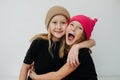 Friendly siblings in colorful hats hugging, touching their cheeks.