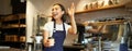 Friendly smiling barita girl waving at client, holding their cup of coffee, prepared takeaway order, working in cafe Royalty Free Stock Photo