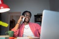 Friendly young African man freelance consultant talking to client on phone while working from home Royalty Free Stock Photo