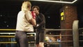 Friendly trainer teaching fit girl on boxing ring. Opponents boxing at gym